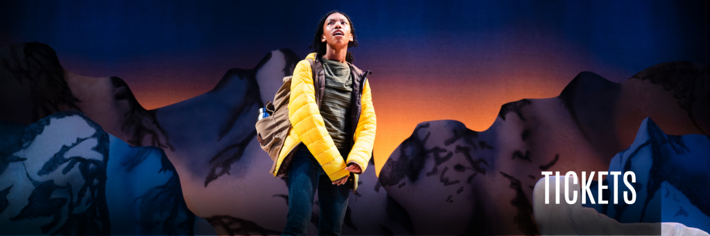 Guest Artist Téa Guarino in Connecticut Rep's A Hundred Words for Snow (Fall 2023) standing in a yellow puffer jacket in front of snow-capped mountains. "TICKETS" in text.