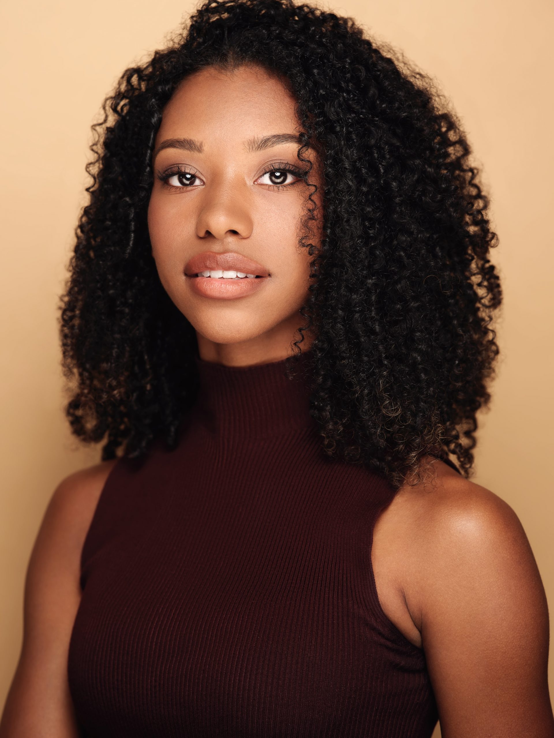 Portrait of Téa Guarino, a young black woman wearing a dark high-collared sleeveless top. 