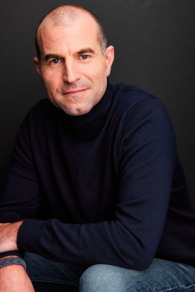 Portrait of Noah Ilya Alexis Tuleja, a balding white man wearing a black turtleneck.