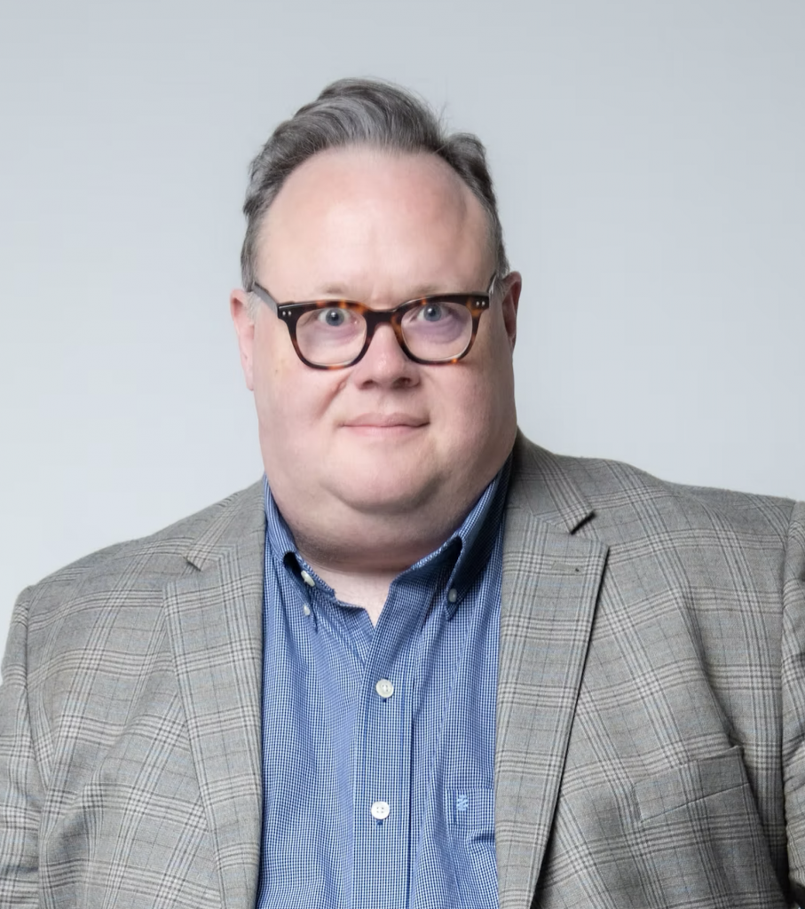 Portrait of Freddy Ashley, a white man wearing thick rimmed glasses.