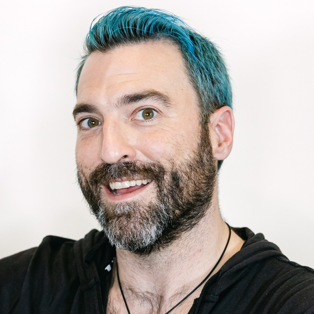A headshot of director Matt Sorensen, a queer man smiling at the camera with blue hair and a brown beard wearing a black shirt and necklace against a white background.