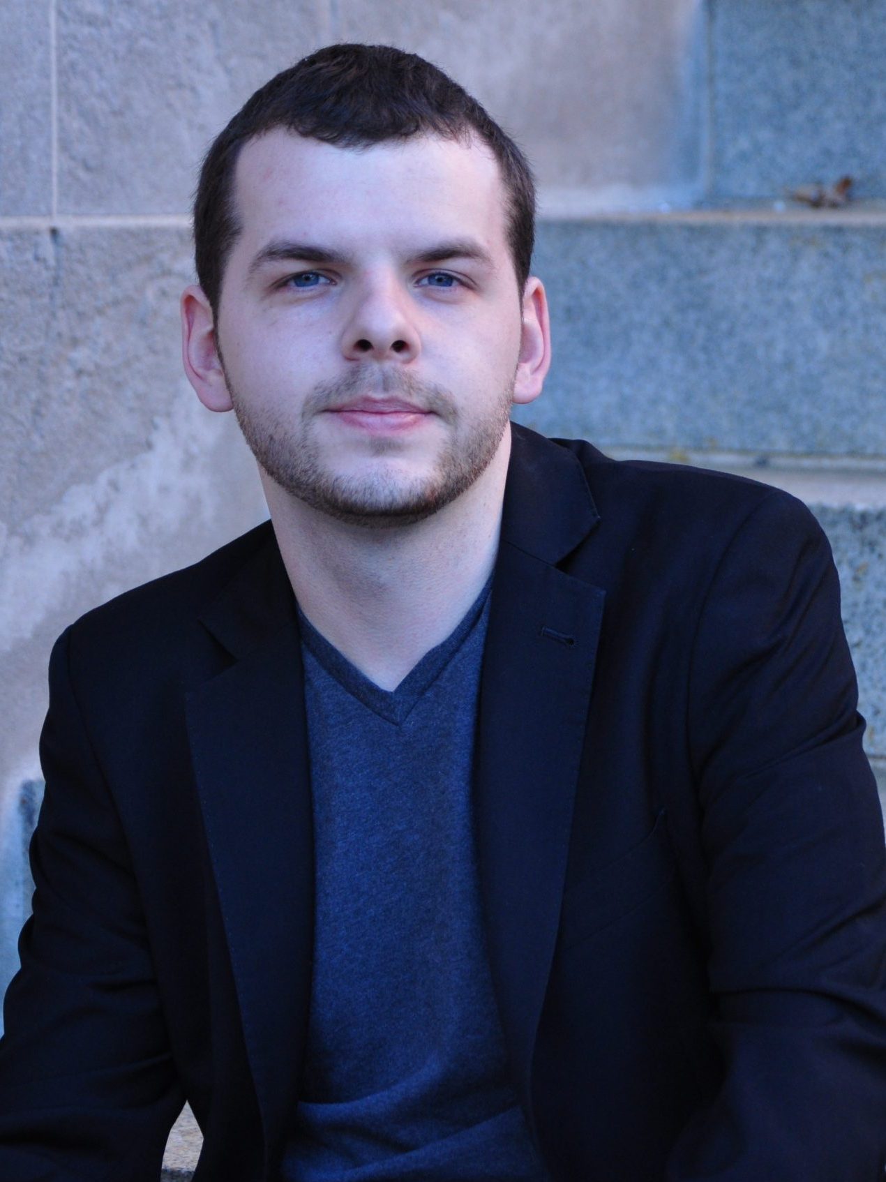 Portrait of Dmitriy Glivinskiy, a Ukrainian. man with short dark hair, wearing a dark jacket over a blue tee-shirt.