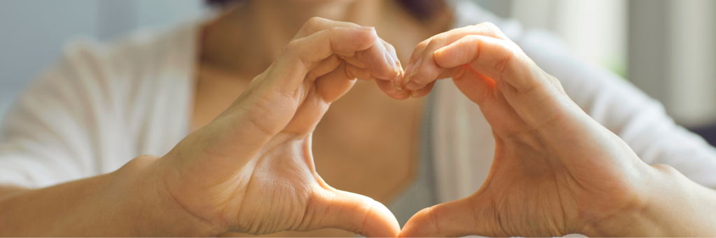 A person creating a heart with their hands in front of their body.