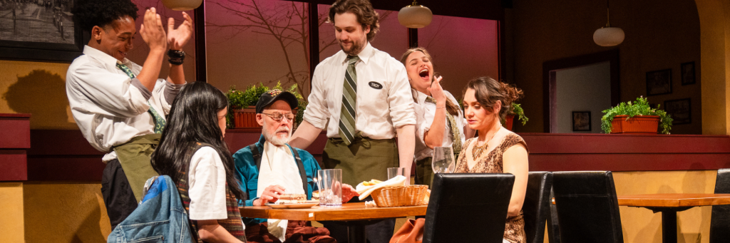 In a scene from CRT's 2025 production of Pocatello, the cast gathers around the table in a typical Italian chain restaurant to sing Happy Birthday to an unwilling customer.