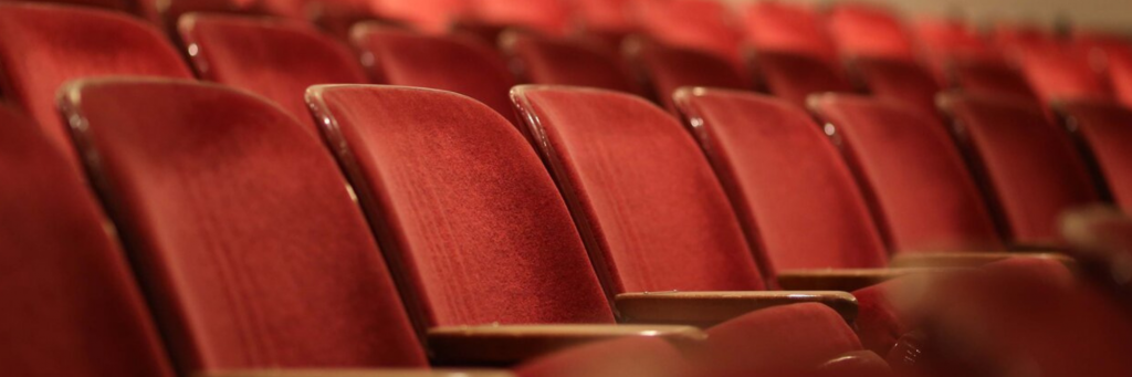 Rows of empty, red velvet seats in a theater.