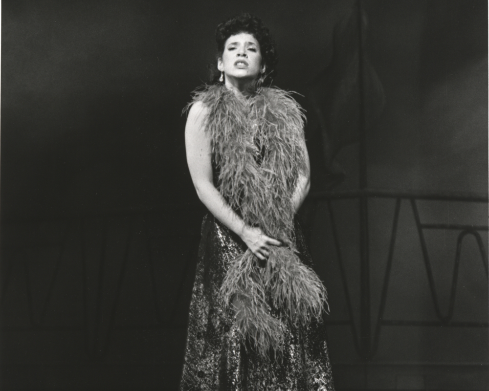 A dark haired chanteuse wearing a feathered boa